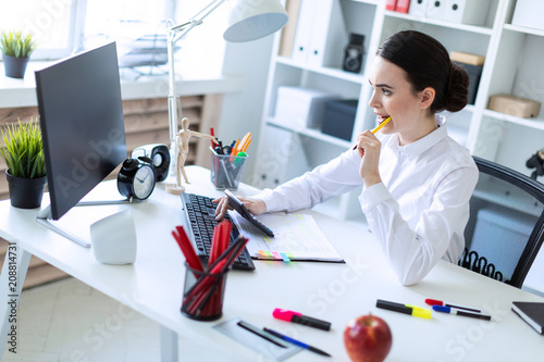 A young girl in the office holds a pen in her mouth and works with a calculator, documents and a computer. photo