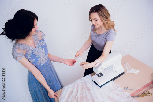 beautiful woman seamstress with long hair and customer. tailor creates image for customer in sewing workshop. dressmaker measures girl with measuring tape . Concept Fashion Design photo