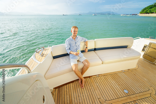 Luxury traveling. Handsome young confident man sitting on the deck of modern yacht. © luengo_ua