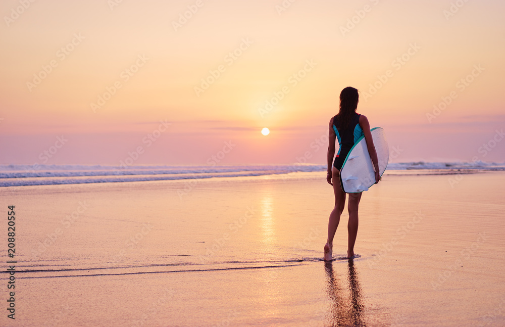 Hobby and vacation. Sunset on the beach. Young woman carrying surf board.