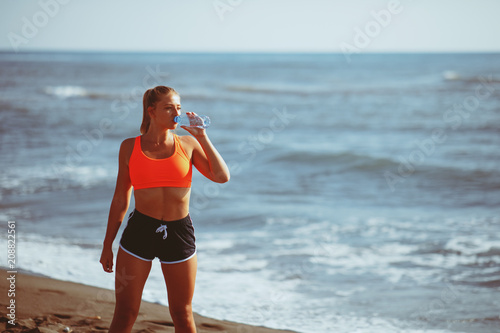 Young fitness woman drinking water by the sea
