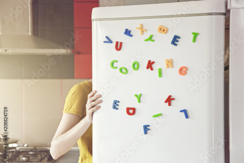 Woman looking in open fridge with Cooking  letters on door. Cooking for family and children concept
