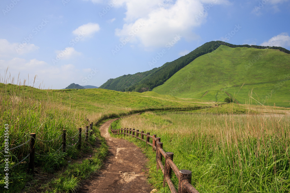 Winding dirt trail with wooden fence leads up steep grassy hill in Soni Kogen