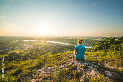 Quadro em tela A Girl Sits on the Edge of the Cliff and Looking at the Sunset and the Valley wi