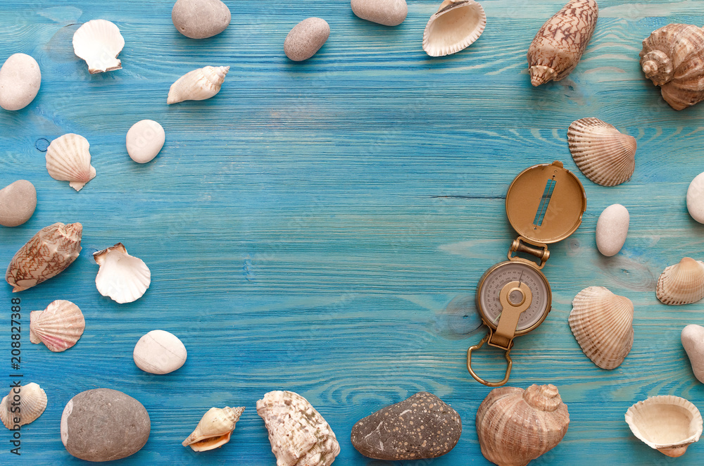 Summer vacation background with copy space. Verious seashells and pebbles border frame and compass on blue wooden table background.
