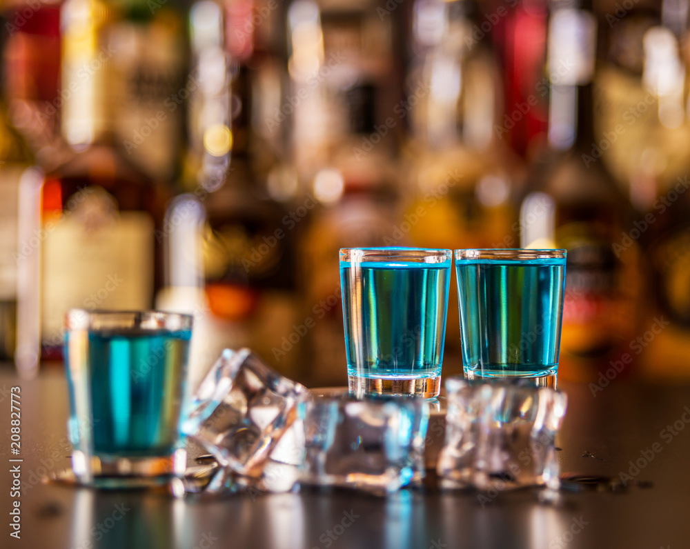 Popular blue drink shot kamikaze on the background of the bar with bottles, a refreshing drink Popular blue drink shot kamikaze on the background of the bar with bottles, a refreshing drink