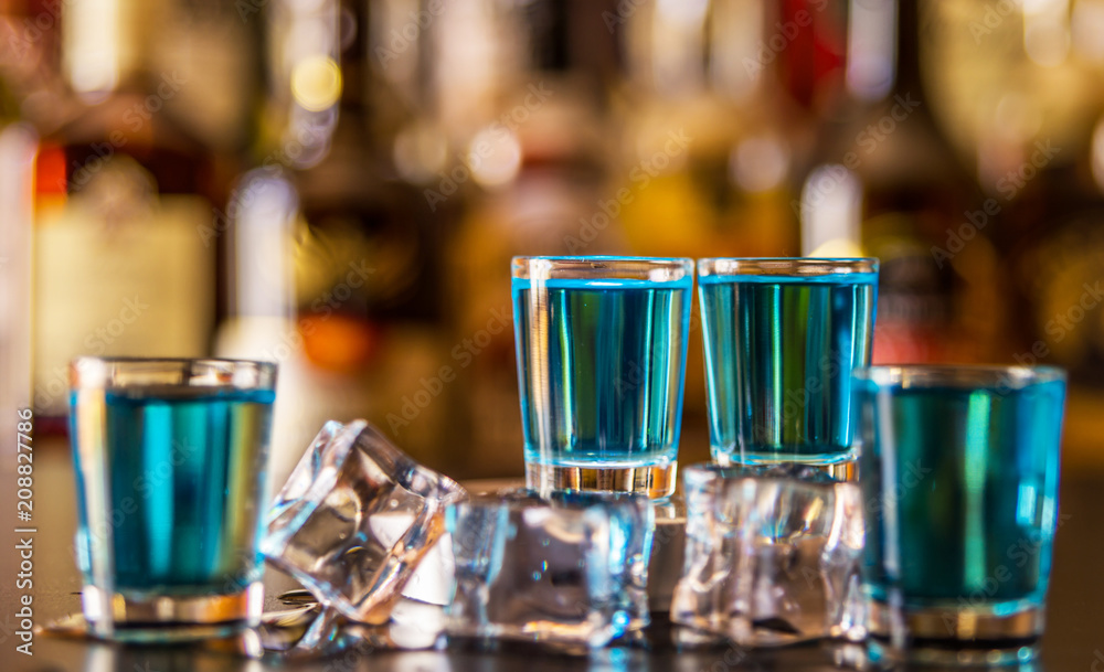 Popular blue drink shot kamikaze on the background of the bar with bottles, a refreshing drink Popular blue drink shot kamikaze on the background of the bar with bottles, a refreshing drink