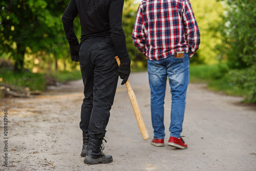 An offender in black clothes with a baseball bat in his hands attacks a man. Pickpocketing on the street during daytime. An offender in black clothes with a baseball bat in his hands attacks a man. Pickpocketing on the street during daytime.