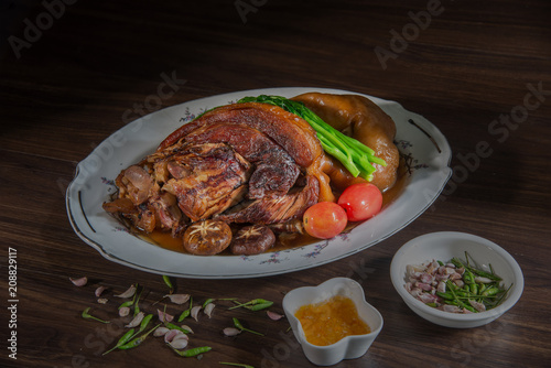 Stewed pork leg in gravy sauce and vegetable on white dish on wooden background with dim light. Chinese food. Still Life image and Selective focus.