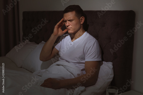 Handsome young man suffering from headache while sitting in bed at night