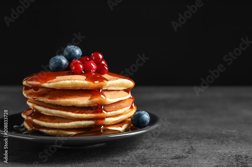 Stack of tasty pancakes with berries and syrup on table