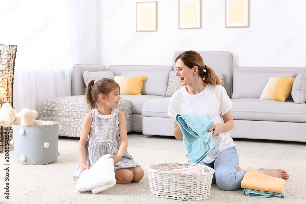 Housewife with daughter folding freshly washed towels in room Housewife with daughter folding freshly washed towels in room