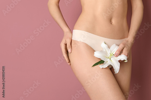 Young woman with flower showing smooth silky skin after epilation on color background