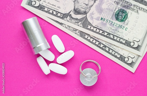 Metal container for pills and money on a pink background, concept of expensive drugs, close-up photo