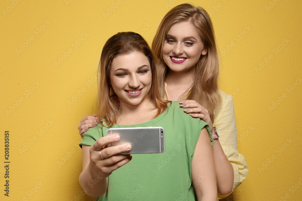 Attractive young women taking selfie on color background Attractive young women taking selfie on color background