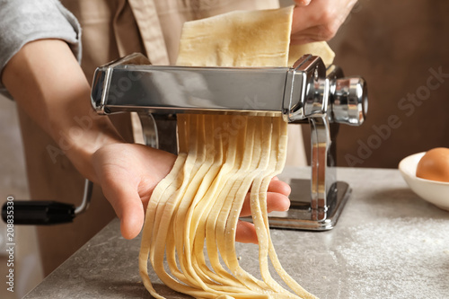 Slika na platnu Young woman preparing noodles with pasta maker at table