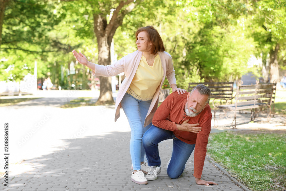 Woman helping mature man suffering from heart attack in park