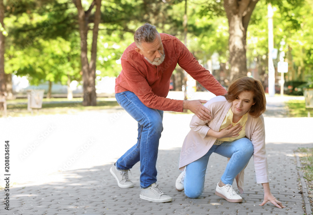 Fototapeta premium Man helping mature woman suffering from heart attack in park