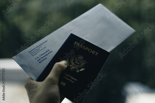 Fotografi Envelope from USCIS (United states citizenship and immigration Services) and Passport of USA in Hand, blurred toned on green and white background