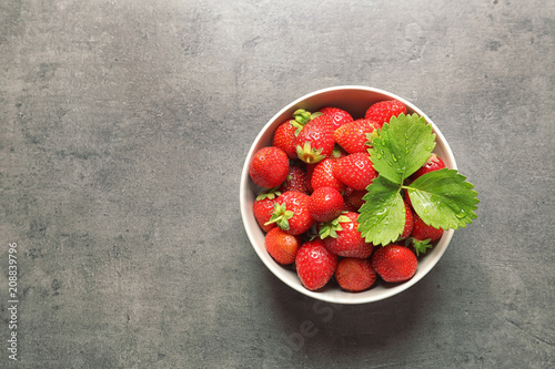 Bowl with ripe strawberries on grey background, top view