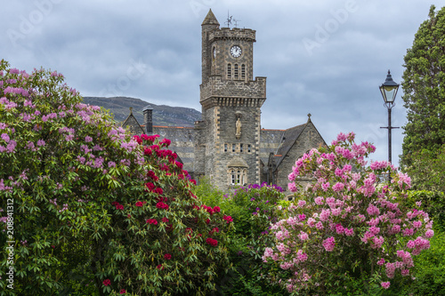 Fort Augustus, Scotland - June 11, 2012: Closeup of the Abbey Highland Club clock tower with flowers fronted by garden under heavy cloudscape. 