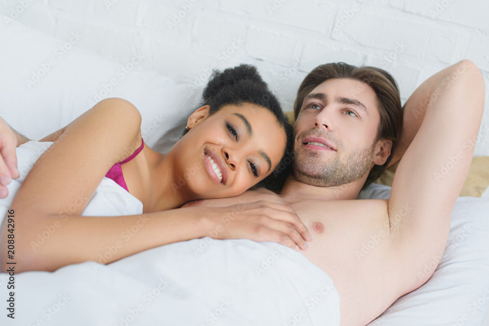 portrait of young smiling interracial couple lying in bed in morning at home portrait of young smiling interracial couple lying in bed in morning at home