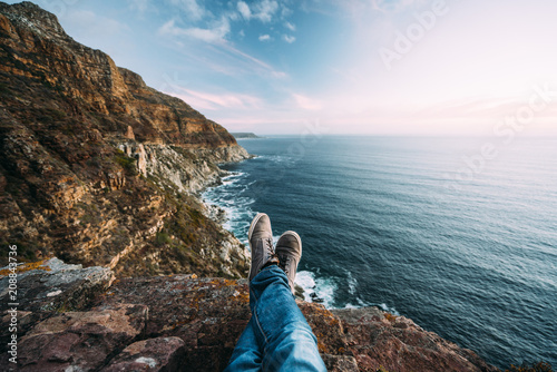 Point of views of crossed legs and shoes with a scenic view mountains, coast and sea at sunset photo
