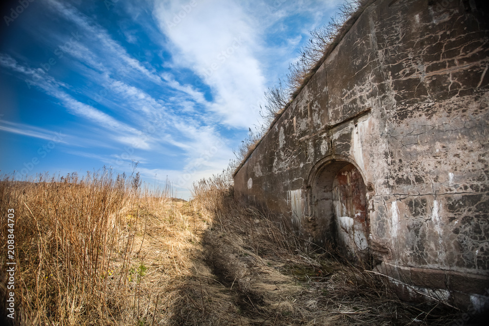 old destroyed wall with deepening in the field of dried grass and blue sky with clouds
