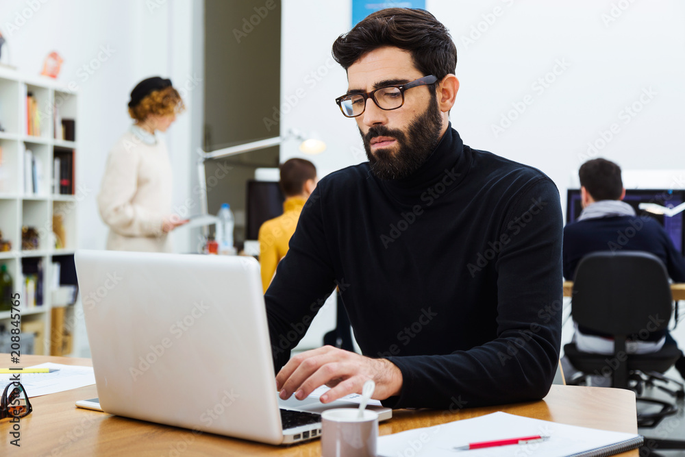 Bearded entrepreneur working on laptop in office. Bearded entrepreneur working on laptop in office.