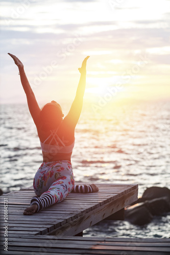 woman playing yoga pose on beach pier against sun rising sky