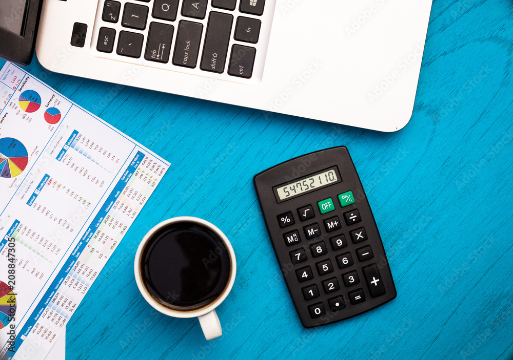 Investment, finance and work concept with charts and graphs and laptop, coffee, calculator on blue board flat lay Investment, finance and work concept with charts and graphs and laptop, coffee, calculator on blue board flat lay