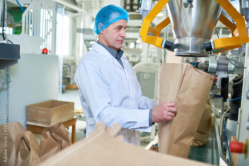 Side view portrait of senior factory worker filling paper bags in packaging section of modern food factory, copy space Side view portrait of senior factory worker filling paper bags in packaging section of modern food factory, copy space