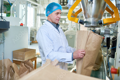 Side view portrait of senior factory worker filling paper bags in packaging section of modern food factory, copy space