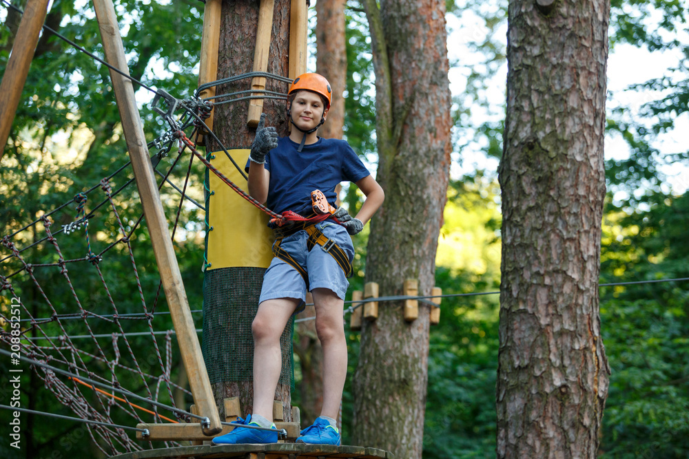 Happy, cute, young boy in blue t shirt and helmet having fun and playing at adventure park, holding ropes and climbing wooden stairs. active lifestyle concept