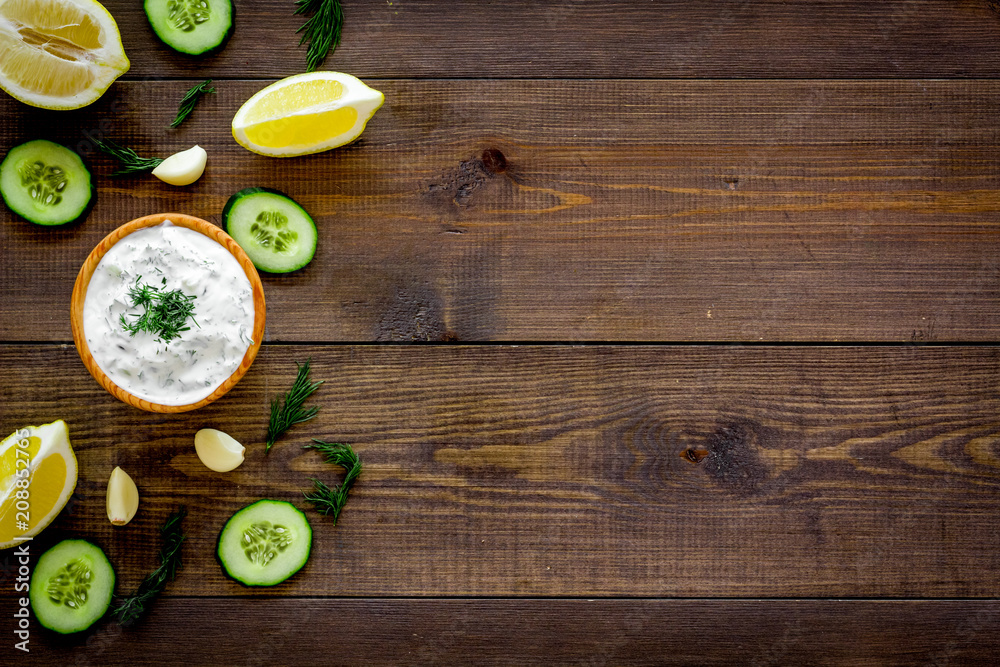 Greek yogurt dip with greenery, cucumber, oranges, garlic on dark wooden background top view space for text pattern, frame Greek yogurt dip with greenery, cucumber, oranges, garlic on dark wooden background top view space for text pattern, frame