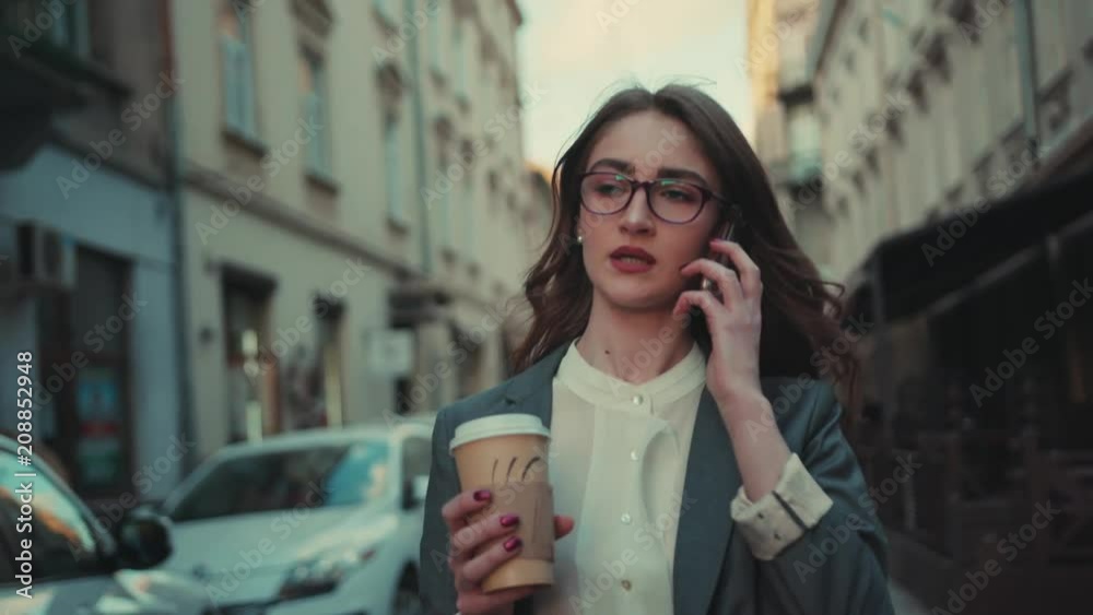 Hot young woman in a stylish glasses walks down the street with coffee, gets a call, answers the phone. Modern lifestyle, active, success. Female portrait Hot young woman in a stylish glasses walks down the street with coffee, gets a call, answers the phone. Modern lifestyle, active, success. Female portrait