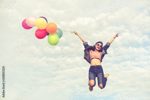 Pretty Asian girl jumping and hand holding colorful balloons on blue sky background for birthday, wedding honeymoon and cerebration party in vintage retro style.