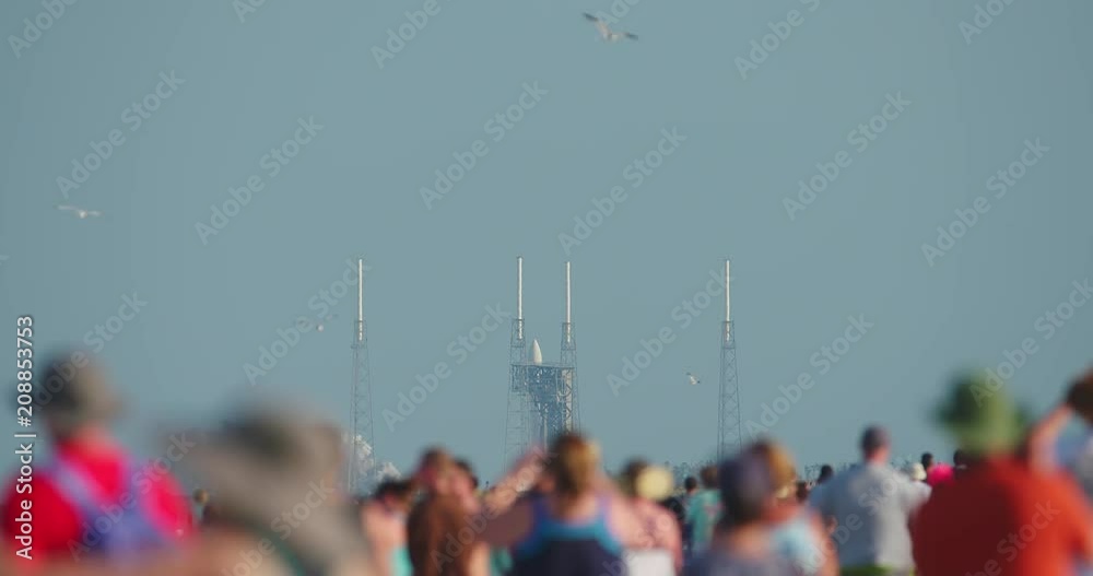 Crowd watches as a NASA SpaceX rocket launches into the sky with lots of smoke and flames