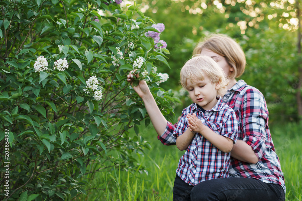 Mother and son in plaid shirts. Woman and boy are standing by flowering bush of lilac. Family time together. Mother and son in plaid shirts. Woman and boy are standing by flowering bush of lilac. Family time together.