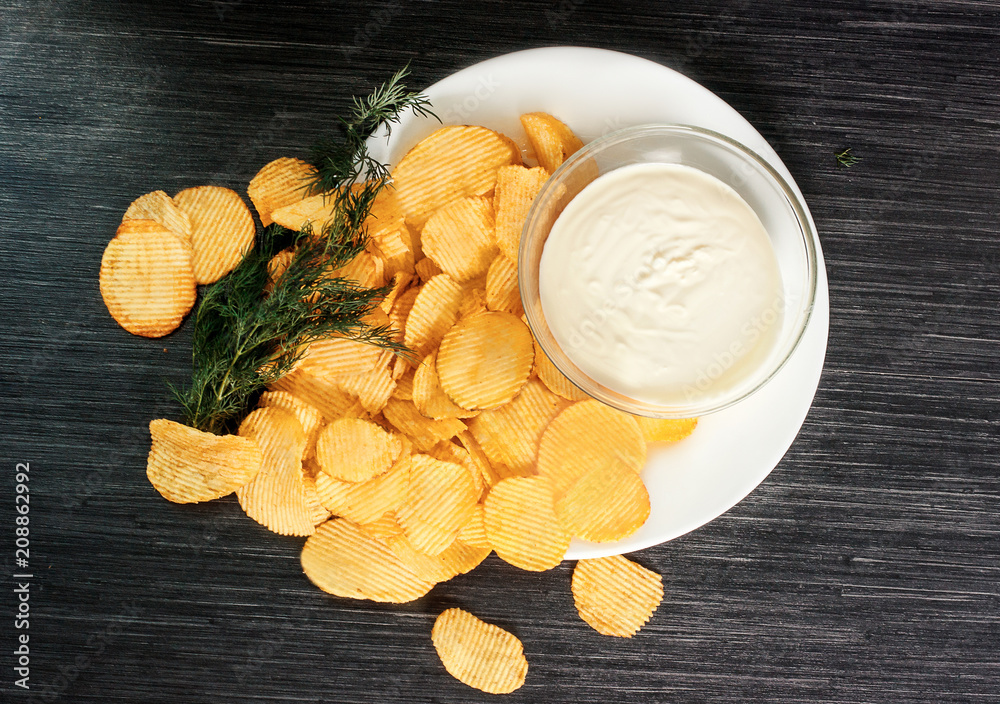Potato chips with sprig of dill and bowl of sour cream on a white plate. Fast food. Rustic food background.  Top view