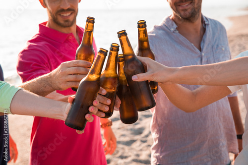 Cheers! Group of happy young people are toasting with bottles of beer in the beach. Celebration concept