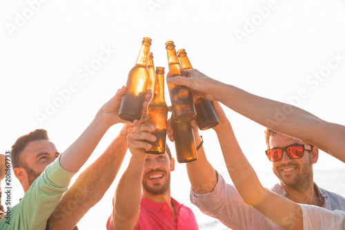 Cheers! Group of happy young people are toasting with bottles of beer in the beach. Celebration concept photo