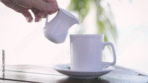 Male hand pouring milk in white cup of coffee on blurred palm tree on the background. slow motion. 3840x2160 photo