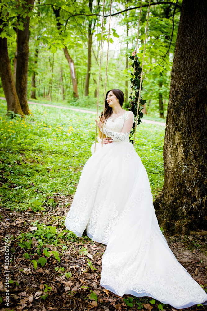 The bride is sitting on a swing decorated with flowers in the park The bride is sitting on a swing decorated with flowers in the park