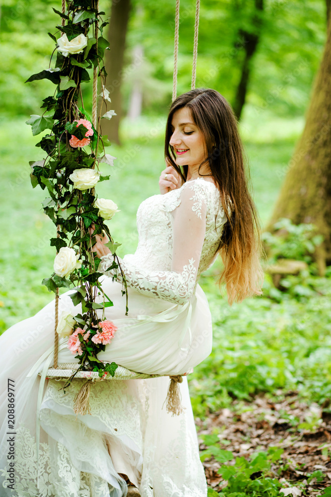 Beautiful bride is sitting on a swing decorated with flowers in the park Beautiful bride is sitting on a swing decorated with flowers in the park