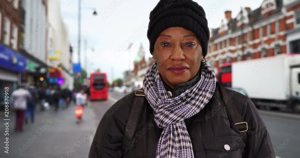 Elderly black woman in a coat and scarf stands on London street, Portrait of senior African American woman smiling at camera, 4k Elderly black woman in a coat and scarf stands on London street, Portrait of senior African American woman smiling at camera, 4k