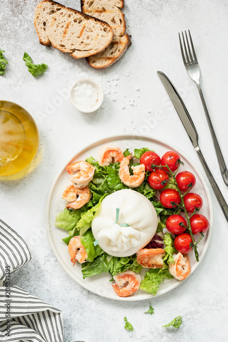 Healthy salad with burrata  shrimps  tomato and lettuce on white plate. Top view of tasty italian salad with olive oil dressing. Healthy eating concept