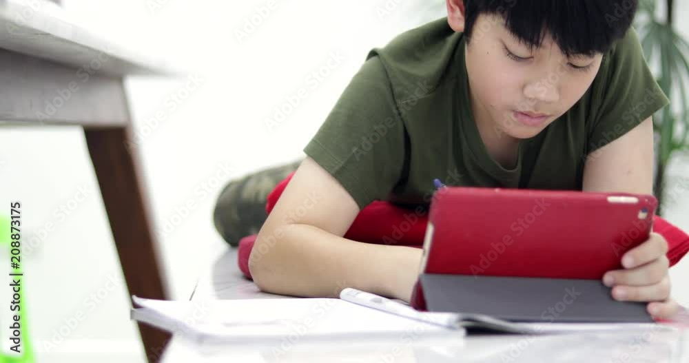 Asian boy doing your homework with tablet computer and headphone at home. Dolly move right to left. Asian boy doing your homework with tablet computer and headphone at home. Dolly move right to left.