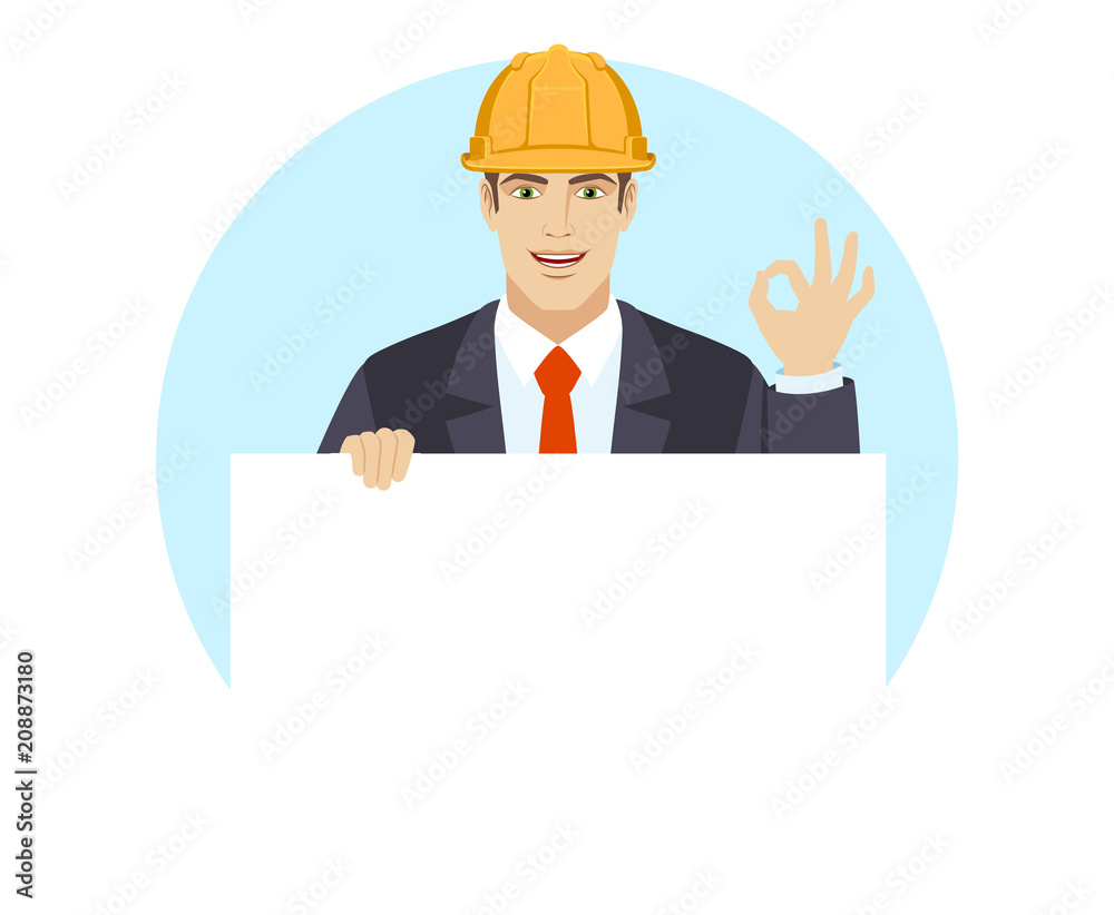 OK! Businessman in construction helmet holding white blank poster and showing a okay hand sign OK! Businessman in construction helmet holding white blank poster and showing a okay hand sign