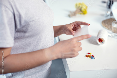 Useful medication. Close up of attractive female hands holding plastic and pills lying on table